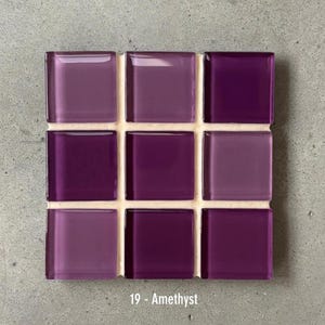 May include: A square mosaic tile sheet featuring nine glass tiles in varying shades of purple. The tiles are arranged in a 3x3 grid and are labeled "19 - Amethyst". The tiles are mounted on a white backing.
