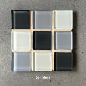 May include: A square mosaic tile sample with nine glass tiles in shades of black, gray, and white. The tiles are arranged in a 3x3 grid and are labeled "58 - Stone". The tiles are set on a beige backing.