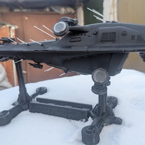 May include: A black spaceship model with a detailed design, mounted on a black stand. The spaceship has multiple antennas and a textured surface.