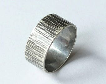 May include: A silver ring with a textured, brushed finish. The ring is wide and has a rounded edge.