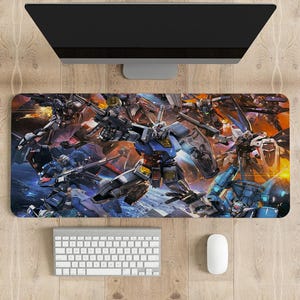 Puede incluir: Alfombrilla de ratón rectangular con una vibrante ilustración de múltiples mechas Gundam en una escena de batalla dinámica. El diseño muestra robots en tonos azules, grises y amarillos sobre un fondo de explosiones. Un teclado y un ratón blancos están debajo de un monitor de ordenador.