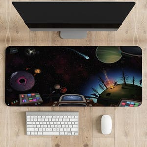 Pode incluir: Tapete de mesa com uma ilustração colorida com tema espacial. O design apresenta planetas, estrelas e um astronauta de desenho animado. Um teclado, um rato e um monitor estão posicionados acima.