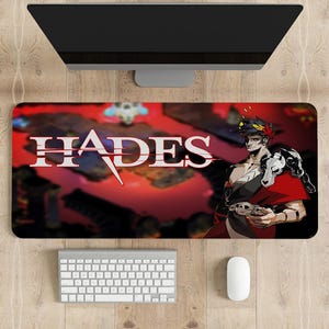 May include: A red and black gaming mouse mat with the word "Hades" in white text and a character from the game Hades. The character is a man wearing a red and black outfit and holding a sword.
