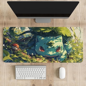 May include: A rectangular desk mat featuring a vibrant illustration of a teal Bulbasaur creature resting in a lush green forest setting. The artwork includes a small red and white Poké Ball icon on the left side, surrounded by detailed foliage.
