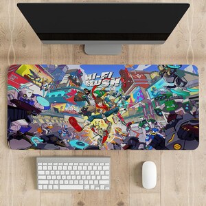 Puede incluir: Una alfombrilla de ratón rectangular de Hi-Fi Rush con una ilustración vibrante y llena de acción con personajes y el logotipo del juego. El diseño incluye una variedad de robots y figuras coloridas en una escena dinámica de estilo cómic. También se ven un teclado, un ratón y un monitor.