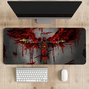 May include: A red and black Deadpool character with wings made of blood is depicted on a gray and red gaming mouse pad. The mouse pad is on a wooden surface with a white keyboard and mouse.
