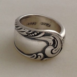 May include: A silver spoon ring with an ornate design. The ring is engraved with the words "Love Grandma".