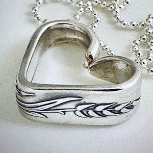 May include: A silver heart-shaped pendant necklace with a wheat design. The pendant is open in the center and hangs from a silver chain.