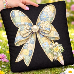 Könnte beinhalten: Schwarzes quadratisches Kissen mit einem großen Schleifendesign mit Perlenmitte und einem Blumenstrauß. Die Schleife besteht aus Patchwork-Stoff in Pastellfarben, darunter Blau, Gelb und Grün. Das Kissen wird von einer Person gehalten.