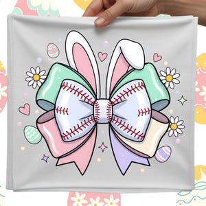 以下が含まれることがあります： 野球をテーマにしたイースターデザインの灰色の正方形の布。赤いステッチの野球のリボン、ウサギの耳、パステルリボン、イースターエッグ、デイジー、ハート、星が特徴です。布は手で持たれています。