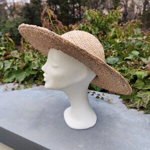 May include: A wide-brimmed straw hat with a natural woven texture. The hat is displayed on a white mannequin head, showcasing its shape and design. The hat's brim is wide, providing ample shade. The hat is a fashion accessory.