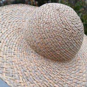 May include: A woven straw hat with a wide brim and a rounded crown. The hat is made of natural-colored straw and has a textured appearance. The brim is wide, providing ample shade. The hat is a summer accessory.