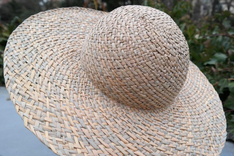 May include: A woven straw hat with a wide brim and a rounded crown. The hat is made of natural-colored straw and has a textured appearance. The brim is wide, providing ample shade. The hat is a summer accessory.