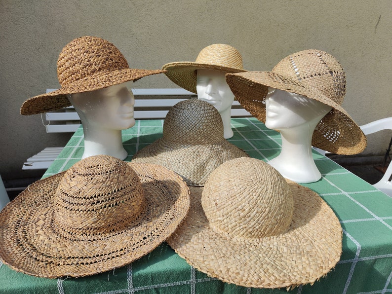 May include: A collection of woven straw hats in various styles, including wide-brimmed sun hats and smaller, more structured designs. The hats are displayed on white mannequin heads, showcasing their shape and texture. The hats are a natural beige color.