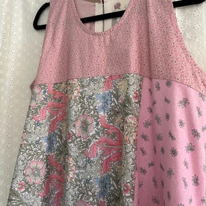 May include: A sleeveless dress with a patchwork design. The top section is a light pink fabric with small dots. The middle section features a floral pattern with pink, blue, and green flowers. The right side is a solid pink with small flower designs.
