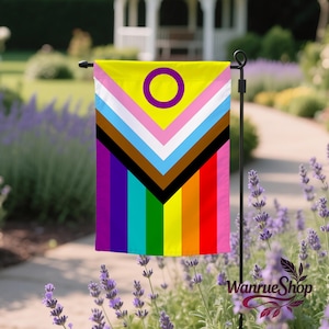May include: A garden flag featuring the Intersex-Inclusive Pride flag. The flag has a yellow top with a purple circle, and a chevron design with pink, white, light blue, brown, and black stripes. The bottom has a rainbow stripe design.