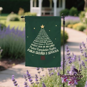 May include: A dark green garden flag with a tree-shaped design made of white text. The text includes phrases like "Protect Reproductive Rights" and "Public Education & Services." A gold star and smaller stars are at the top. The flag is displayed outdoors.