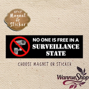 Pode incluir: Um íman ou autocolante retangular preto com um ícone de câmara de segurança branca dentro de um círculo de proibição vermelho. O texto diz NO ONE IS FREE IN A SURVEILLANCE STATE. O produto mede 25,4 cm por 7,6 cm no rótulo.