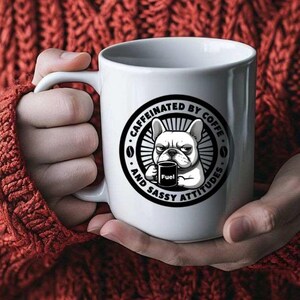 Puede incluir: Taza de café blanca con un gráfico en blanco y negro de un bulldog sosteniendo una taza de café, con el texto "CAFFEINATED BY COFFEE AND SASSY ATTITUDES". La taza tiene un asa curva.