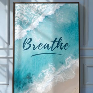May include: Framed wall art featuring an aerial view of ocean waves in shades of turquoise and white, crashing onto a sandy beach. The word "Breathe" is written in a cursive font across the image.