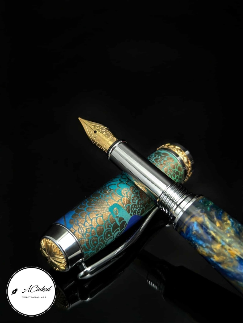May include: A luxury fountain pen with a gold nib and a detailed, ornate design. The pen features a silver body with a cap adorned with teal and gold patterns. The pen is displayed against a black background.