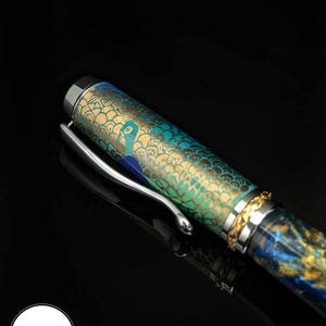 May include: A decorative pen with a peacock design. The pen features a silver clip and a cap with a gold and blue pattern. The barrel of the pen is decorated with a peacock design in shades of green and gold.