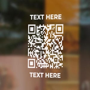 May include: White QR code sticker with the text "TEXT HERE" above and below the code. The sticker is on a glass surface.