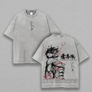 Puede incluir: Camiseta gris con un gráfico de llave en la parte delantera y una ilustración detallada en la parte trasera. El gráfico trasero presenta una figura musculosa con detalles rojos y texto japonés. La camiseta tiene un aspecto vintage.