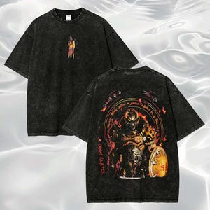 May include: Black, oversized t-shirt with a faded, vintage appearance. The front has a colourful abstract design, and the back shows a detailed illustration of a character with a shield and text. The shirt has short sleeves and a crew neck.