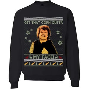 Może przedstawiać: Czarna bluza z portretem mężczyzny i napisem "GET THAT CORN OUTTA MY FACE!". Projekt zawiera płatki śniegu, renifery i dekoracyjną obwódkę, tworząc świąteczny, świąteczny wygląd.