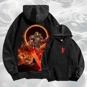 May include: Two black hoodies. One features a large graphic of a futuristic warrior with a glowing red sword against a fiery backdrop. The other has a red symbol on the chest. Both have hoods and front pockets.