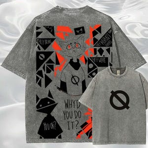 May include: Grey t-shirts with graphic designs. One shirt features a black symbol and the other has a cat-like figure with text that reads "WHY'D YOU DO IT?" and "YOU OK?" The back of the shirt has a cat graphic and text.