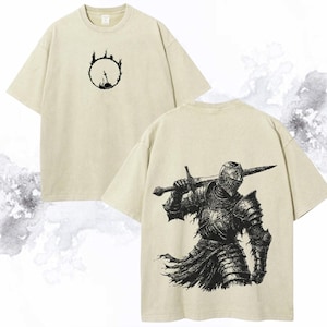 May include: Beige t-shirts with short sleeves. One shirt features a black graphic of a sword in a circle on the front. The other shirt has a detailed black illustration of a knight holding a sword on the back.