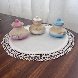 Puede incluir: Una taza de cerámica blanca con asa negra y el texto "But First, Coffee" en negrita negra. La taza se encuentra sobre un fondo borroso, resaltando su diseño limpio.