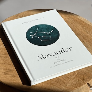 Könnte beinhalten: Ein weißes Buch mit dem Namen "Alexander" in schwarzer Schrift. Auf dem Einband befindet sich ein türkisfarbener Kreis mit einem Sternbilddesign. Das Buch liegt auf einer Holzoberfläche. Der Text "astro impulses" befindet sich oben rechts.