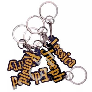 May include: Four keyrings with silver rings and black and gold name tags. The names on the tags are "Jessica", "Joseph", "Edward", and "Raymond".