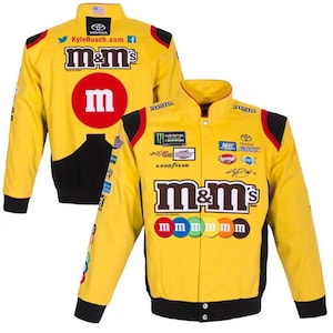 Könnte beinhalten: Gelbe Rennjacke mit dem M&M's-Logo und verschiedenen Sponsorenlogos. Die Jacke hat schwarze Akzente und einen großen roten Kreis mit einem weißen „m“ auf dem Rücken. Auf der Vorderseite sind das M&M's-Logo und eine Reihe bunter Süßigkeiten abgebildet.