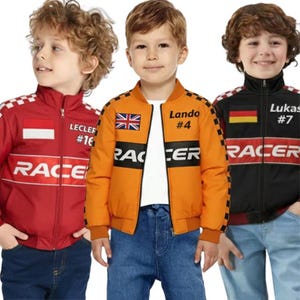 Puede incluir: Tres niños con chaquetas de temática de carreras. Las chaquetas son rojas, naranjas y negras, cada una con "RACER" impreso en el pecho. La chaqueta naranja presenta un parche de la Union Jack y el nombre "Lando #4". La chaqueta roja dice "Lecler #16". La chaqueta negra dice "Lukas #7".