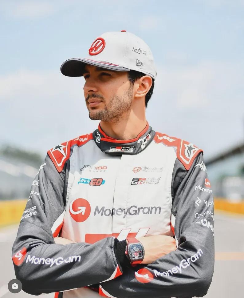 Puede incluir: Una persona con un traje de carreras blanco y gris con detalles rojos, con el logotipo de MoneyGram. La persona tambi&eacute;n lleva una gorra blanca con un logotipo rojo y un reloj negro. El fondo es un circuito.