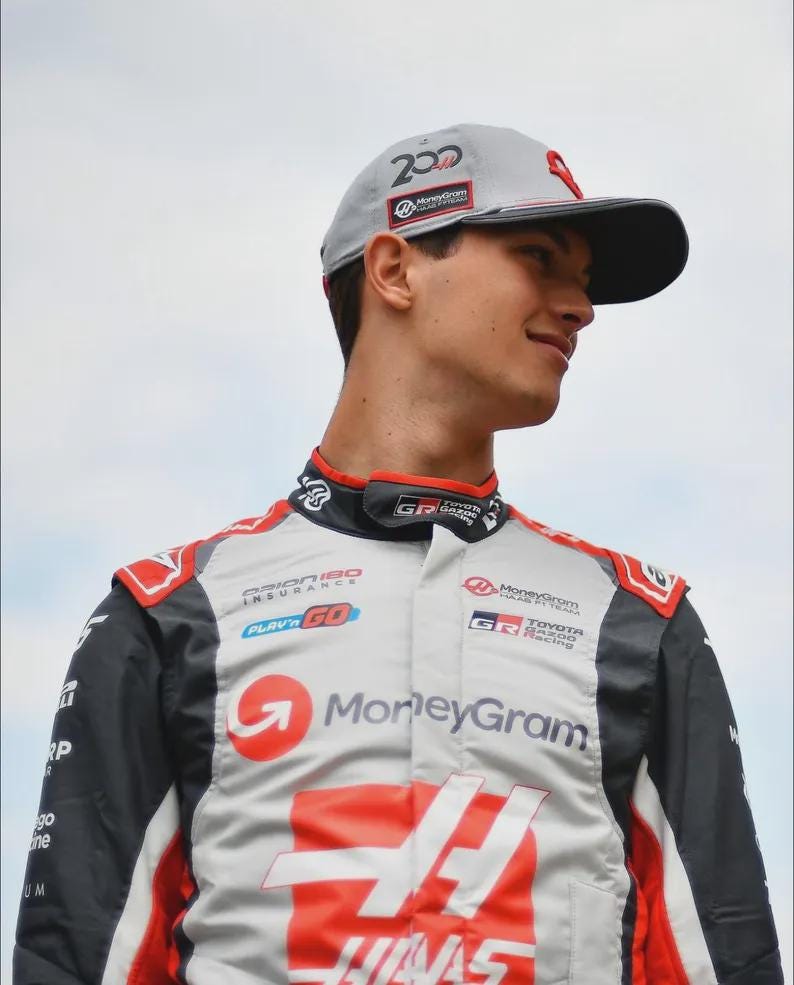 Puede incluir: Gorra de b&eacute;isbol gris claro con visera negra y detalles rojos, con el n&uacute;mero "200" y el logotipo de "MoneyGram". La persona lleva un traje de carreras con los logotipos de "MoneyGram" y "HAAS", y detalles rojos y negros.