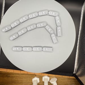 May include: A set of gray plastic measuring tools in the shape of circles with numbers indicating feet. The tools are arranged in a circle on a gray surface. The tools are used to measure distances in feet.