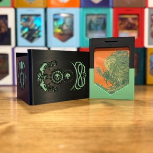 May include: Black card holder with green and white designs, and a card with an orange and green illustration. The holder has a unique design with a skull and other symbols. The card features a detailed drawing of a figure with flowing hair.