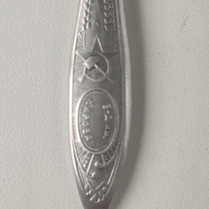 May include: A silver spoon with a wheat design and a hammer and sickle symbol. The spoon has the word "СССР" engraved on it.