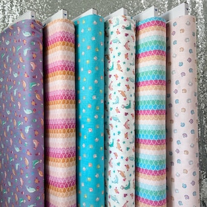 May include: Five rolls of fabric with different patterns featuring dolphins, seashells, and stripes in shades of pink, blue, and white.