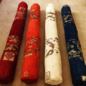 May include: Four decorative cylindrical pillows with floral patterns. The pillows are red, orange, cream, and blue.