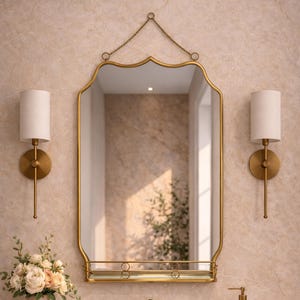 Peut inclure: Une coiffeuse de salle de bain avec un miroir doré, des appliques murales et des robinets assortis. Un vase décoratif de fleurs est posé sur le comptoir. Le miroir est suspendu par une chaîne. L'évier et le comptoir sont en pierre claire.