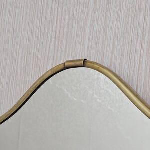 K&ouml;nnte beinhalten: Ein Spiegel im Vintage-Stil mit einer wellenf&ouml;rmigen, unregelm&auml;&szlig;igen Form. Der Rahmen besteht aus goldfarbenem Metall, und die Oberfl&auml;che des Spiegels ist reflektierend. Das Design ist schlicht und elegant, passend f&uuml;r verschiedene Einrichtungsstile.