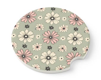 May include: A round, white ceramic coaster with a green background and a pink and white floral pattern. The coaster has a cut-out for a beverage cup.