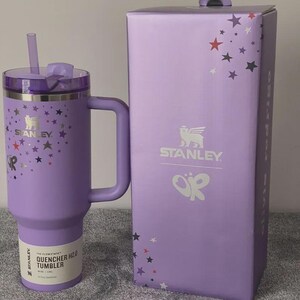 Peut inclure: Un gobelet Stanley Quencher H2.0 lavande avec une poign&eacute;e, une paille et un couvercle, &agrave; c&ocirc;t&eacute; d'une bo&icirc;te assortie. Le gobelet et la bo&icirc;te sont d&eacute;cor&eacute;s de motifs d'&eacute;toiles et du logo Stanley. Le gobelet est con&ccedil;u pour une hydratation tout au long de la journ&eacute;e.