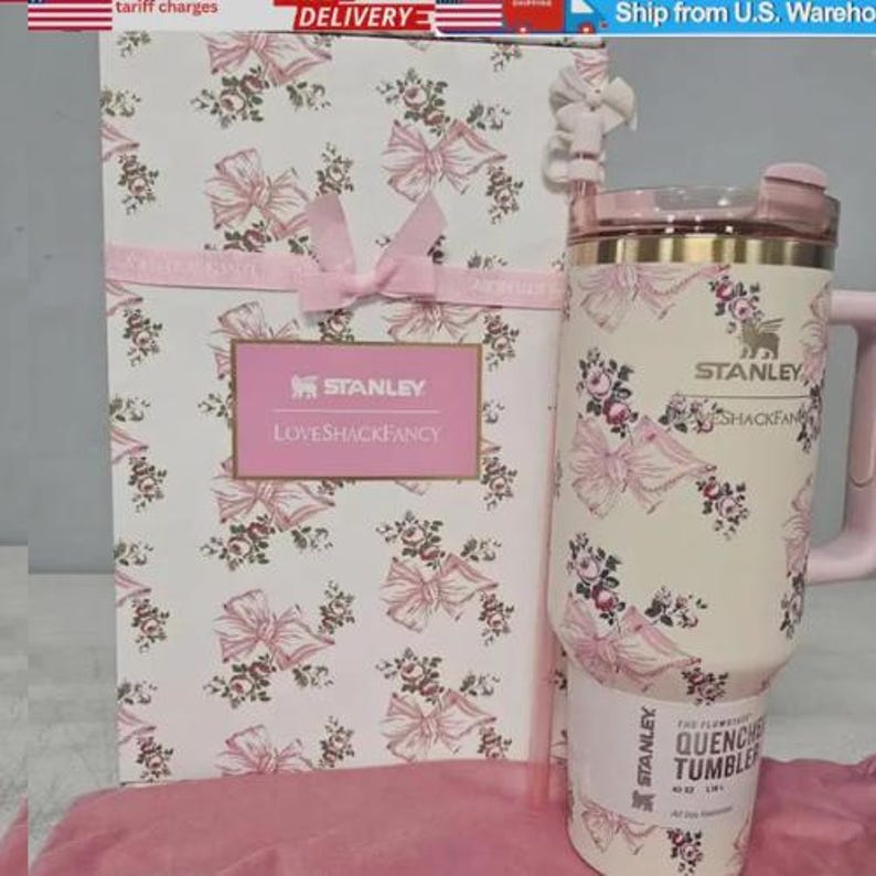 May include: A Stanley Quencher tumbler and gift box, decorated with a pink and cream floral and bow design. The tumbler has a handle and a lid. The gift box features the Stanley and LoveShackFancy logos.